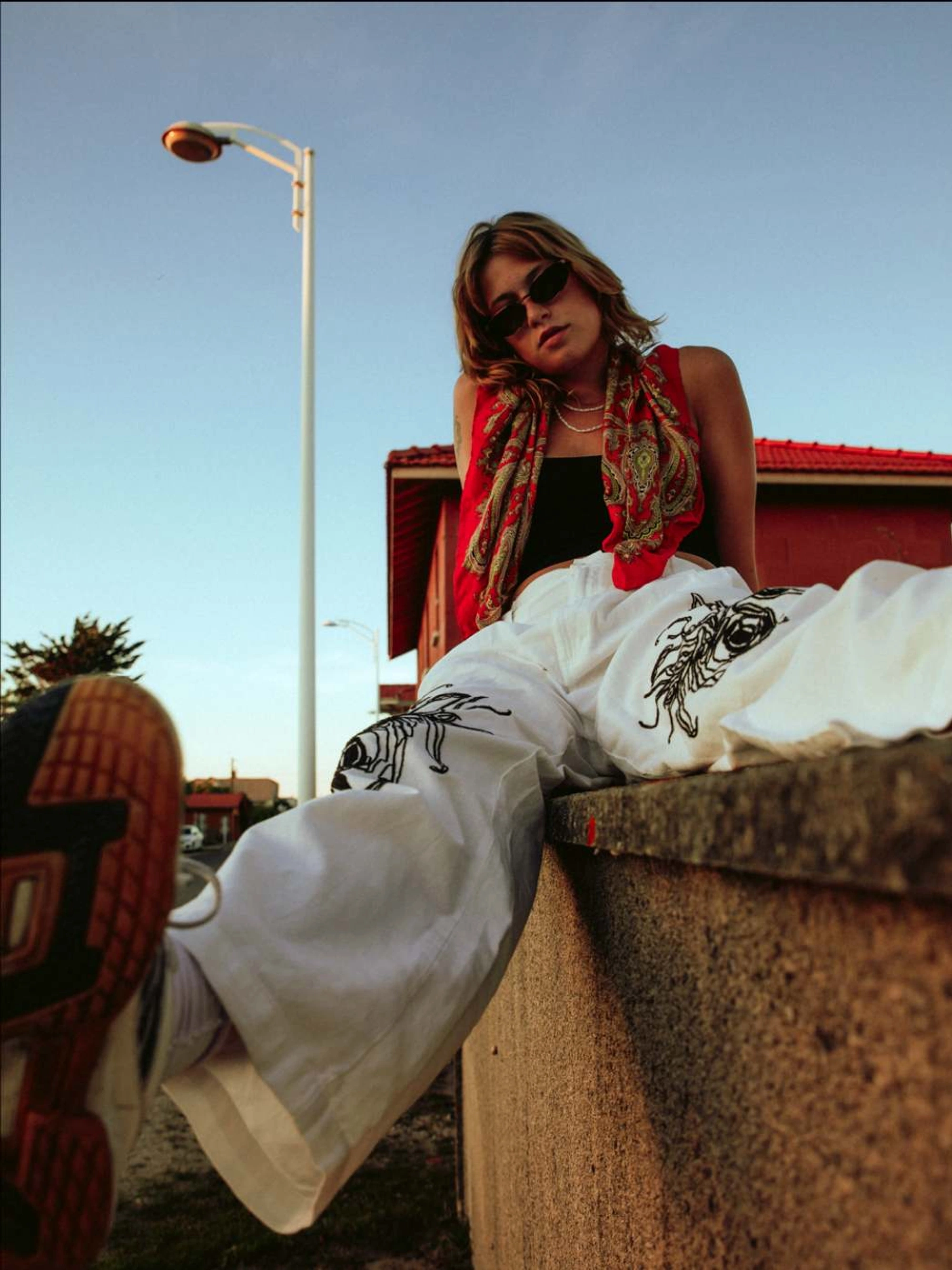 young woman wearing sunglasses sitting on a wall casually