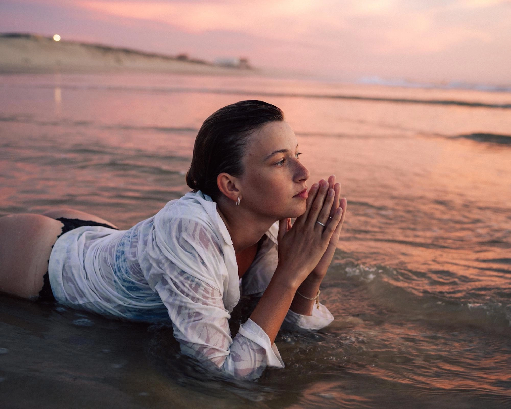 portrait of a young woman lying in the water on the beach while the sun sets