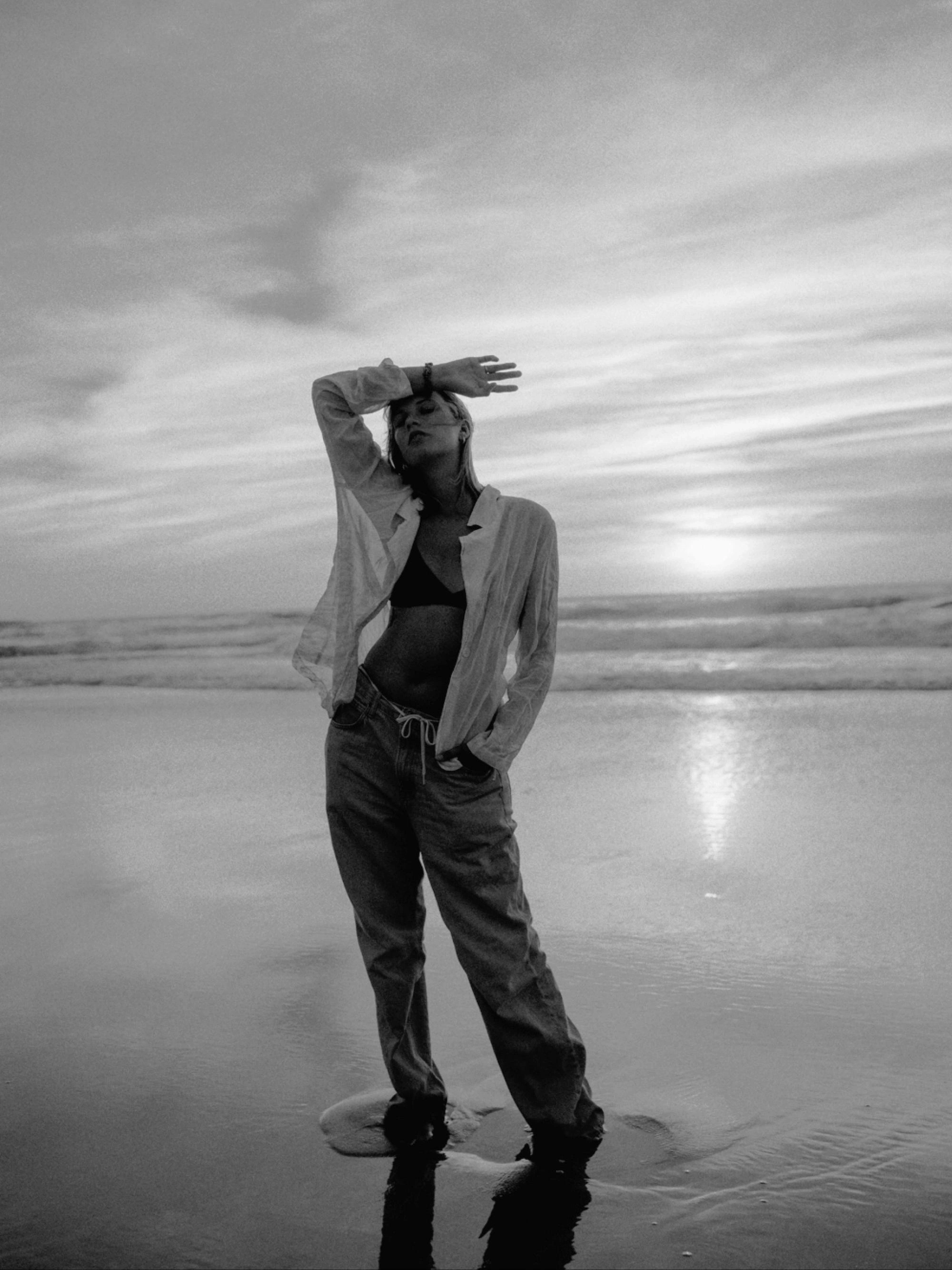 young woman wearing a white shirt and jeans, standing on the beach